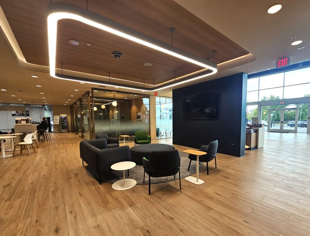 Customer lounge at Young Kia Layton with a wood ceiling feature, illuminated light ring and soft seating