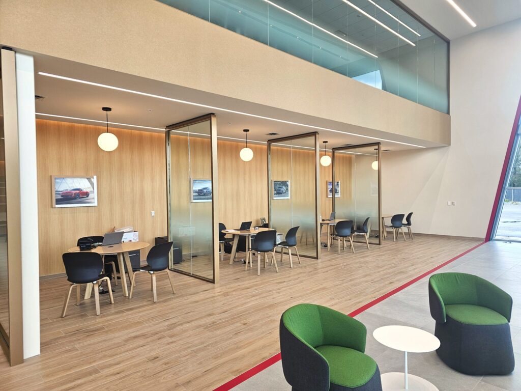 Glass-front sales offices with wood wall panels and pendant lights under the mezzanine at Young Kia Layton