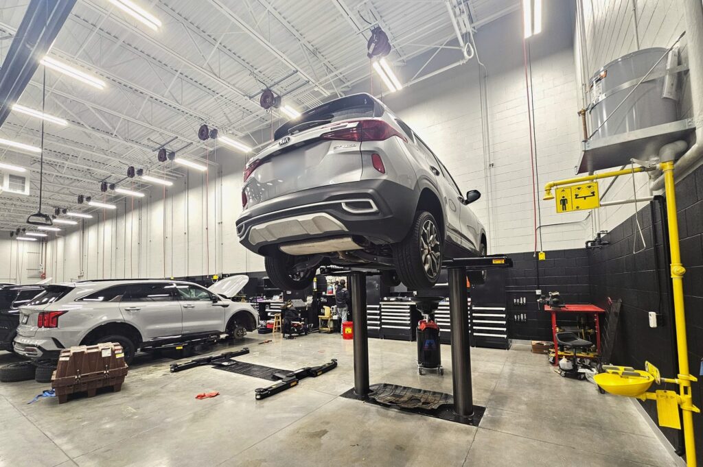 Kia SUV on an in-ground lift in the Young Kia Layton service shop next to an emergency eyewash station