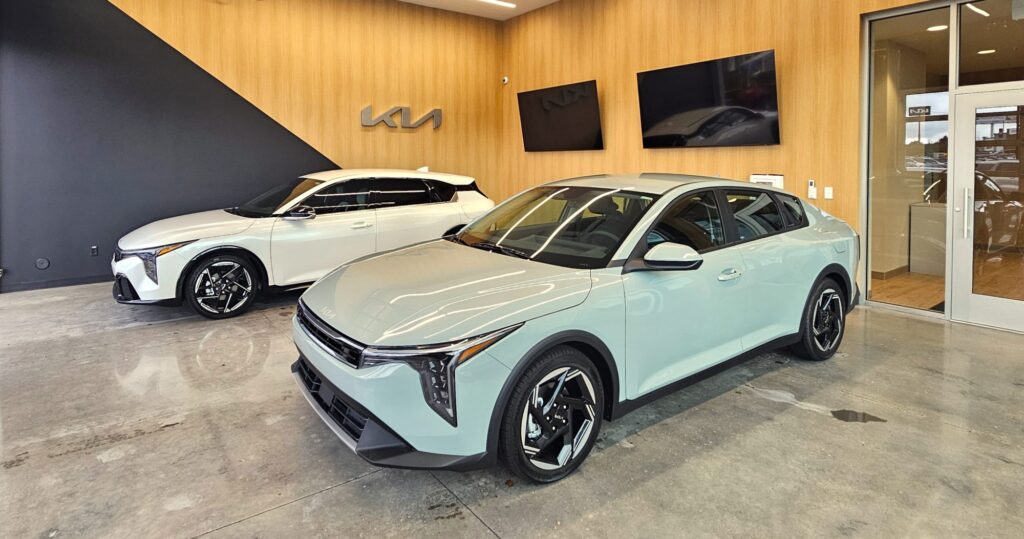 Vehicle delivery bay at Young Kia Layton with two new Kia K4 sedans in front of a wood-paneled wall